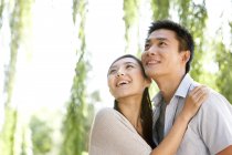 Joven pareja china abrazando y mirando hacia arriba en el parque - foto de stock