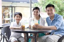 Китайская семья сидит в кафе на тротуаре с холодными напитками — стоковое фото