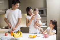 Familia china comiendo frutas en la cocina - foto de stock