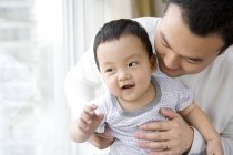 Chinese man holding infant son by window — Stock Photo