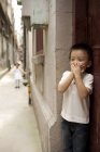 Китайский мальчик, прикрывающий рот во время игры в прятки — стоковое фото