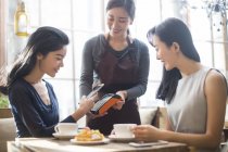 Chinese female friends paying with smartphone in coffee shop — Stock Photo