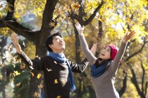 Chinese couple enjoying falling leaves in autumnal park — Stock Photo
