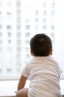 Немовля дивиться крізь вікно, вид ззаду — стокове фото