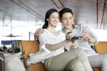 Pareja china sentada con cámara digital en el salón del aeropuerto - foto de stock