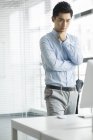 Китайский бизнесмен, стоящий в офисе и смотрящий вниз на компьютер — стоковое фото