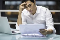 Tired Chinese businessman holding documents in office — Stock Photo