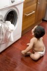 Baby boy sitting on floor and looking at washing machine — Stock Photo