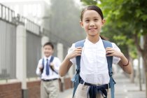 Cheerful schoolgirl with classmate posing on street — Stock Photo