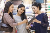 Amigos chineses pagando com smartphone na loja de roupas — Fotografia de Stock