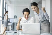 Chinese businesswoman and businessman using laptop and cheering in office — Stock Photo