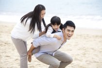 Китайский отец катает дочь на спине по пляжу с матерью — стоковое фото