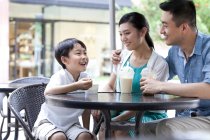 Padres chinos con hijo disfrutando de bebidas frías y helado en la cafetería de la acera - foto de stock