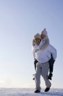 Chinese man carrying woman piggyback on snow — Stock Photo