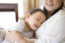 Chinese woman holding infant on chest and smiling — Stock Photo