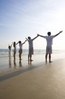 Задний вид семьи из нескольких поколений с поднятыми на пляже руками — стоковое фото