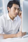 Pensativo empresario chino utilizando la computadora en la oficina - foto de stock