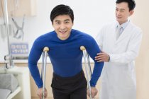 Médico chinês ajudando paciente com muletas — Fotografia de Stock