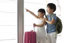 Chinese boy and girl pointing at view at airport — Stock Photo