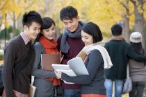 Chinese college students with books talking in campus park in autumn — Stock Photo