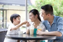 Китайские родители с сыном наслаждаются прохладительными напитками и мороженым в кафе на тротуаре — стоковое фото
