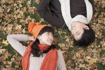 Chinese couple lying amongst maple leaves and sharing earphones — Stock Photo
