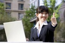 Chinese businesswoman with laptop giving thumbs up on street — Stock Photo