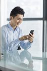 Empresário chinês usando smartphone à mesa no escritório — Fotografia de Stock