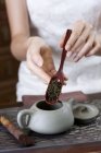Primer plano de las manos femeninas poniendo hojas de té en la tetera - foto de stock