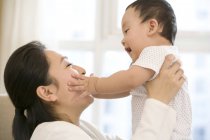 Chinese woman lifting baby boy with arms outstretched — Stock Photo