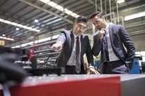Des hommes d'affaires examinent des machines dans une usine industrielle — Photo de stock