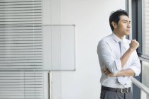 Chinese businessman looking through window in office — Stock Photo