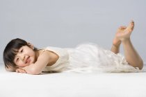 Pequena menina chinesa deitada na frente no fundo cinza — Fotografia de Stock