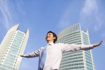Hombre de negocios chino con los brazos extendidos frente al rascacielos - foto de stock