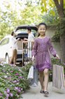 Chica china con bolsas de compras caminando en el patio - foto de stock