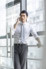 Chinese businessman talking on phone in office building — Stock Photo