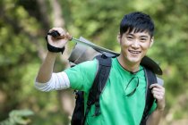 Mochilero masculino chino con poste de senderismo en el bosque - foto de stock