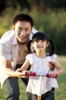 Chinese father teaching daughter riding push scooter — Stock Photo