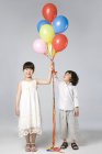 Chinese children holding multi-colored balloons on gray background — Stock Photo