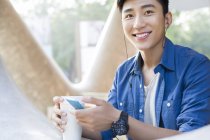Hombre chino escuchando música con smartphone y sosteniendo café - foto de stock