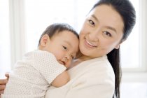 Chinesin hält Säugling auf Brust und lächelt — Stockfoto