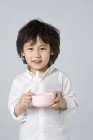 Pequeno menino asiático segurando tigela e colher no fundo cinza — Fotografia de Stock