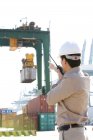 Trabajador de la industria naviera china dirigiendo grúa con walkie-talkie - foto de stock