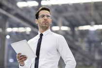 Бізнесмен в захисних окулярах тримає цифровий планшет на заводі — стокове фото