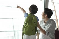 Padre e hijo chinos señalando a la vista en el aeropuerto - foto de stock