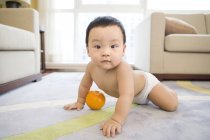 Chinese baby boy crawling and playing with orange fruit — Stock Photo