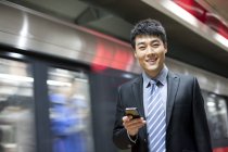 Uomo d'affari cinese che utilizza smartphone alla stazione della metropolitana — Foto stock