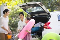 Chinese family putting water sports equipment into car trunk — Stock Photo