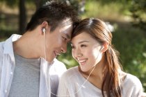 Pareja china compartiendo auriculares y escuchando música en el parque - foto de stock
