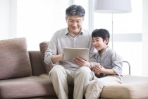 Grand-père et petit-fils chinois utilisant une tablette numérique sur le canapé — Photo de stock